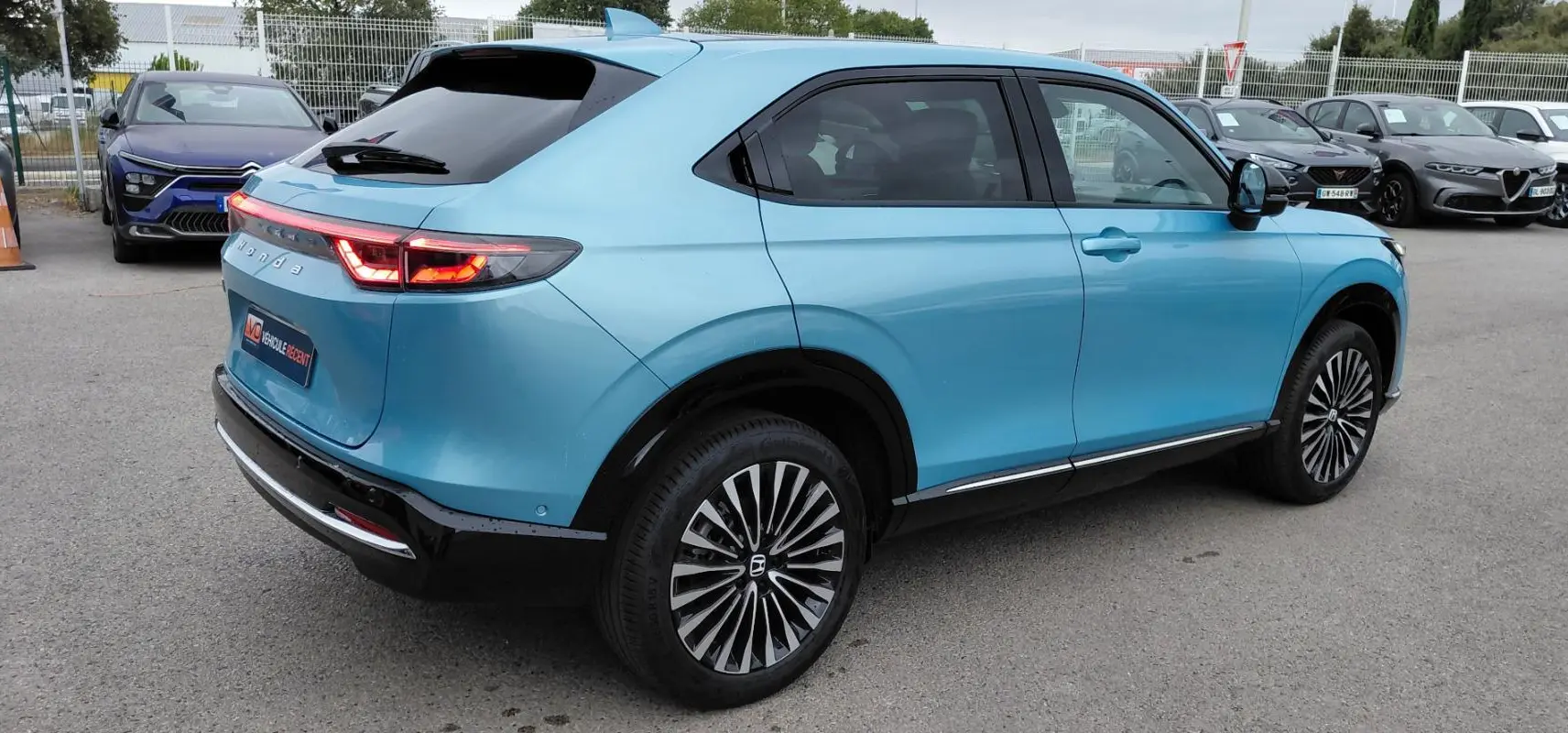 Vue 3/4 arrière droite d'un Honda e:Ny1 bleu électrique 2025 avec feux arrière LED et jantes distinctives.