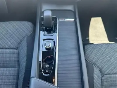 Vue rapprochée de la console centrale noire brillante de la Volvo S60 2024 avec levier de vitesse et accoudoir central entre sièges gris à motifs.