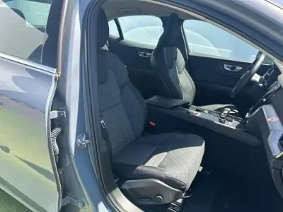 Vue intérieure côté conducteur de la Volvo S60 Thunder Grey Metal 2024, sièges tissu gris et console centrale visible.