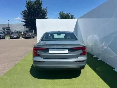 Vue arrière d'une Volvo S60 2024 Thunder Grey Metal stationnée sur gazon synthétique devant un mur blanc.