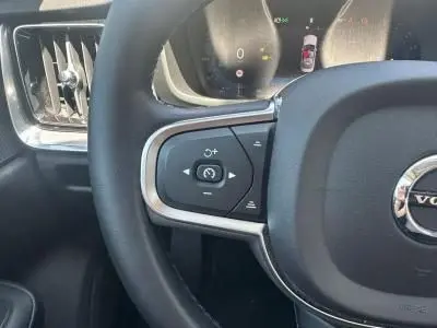 Gros plan sur la partie gauche du volant noir de la Volvo S60 Thunder Grey 2024, avec commandes intégrées et aérateur adjacent.