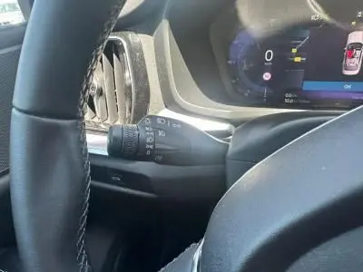 Gros plan sur la manette de clignotant noire à gauche du volant de la Volvo S60 Thunder Grey 2024, tableau de bord digital visible.