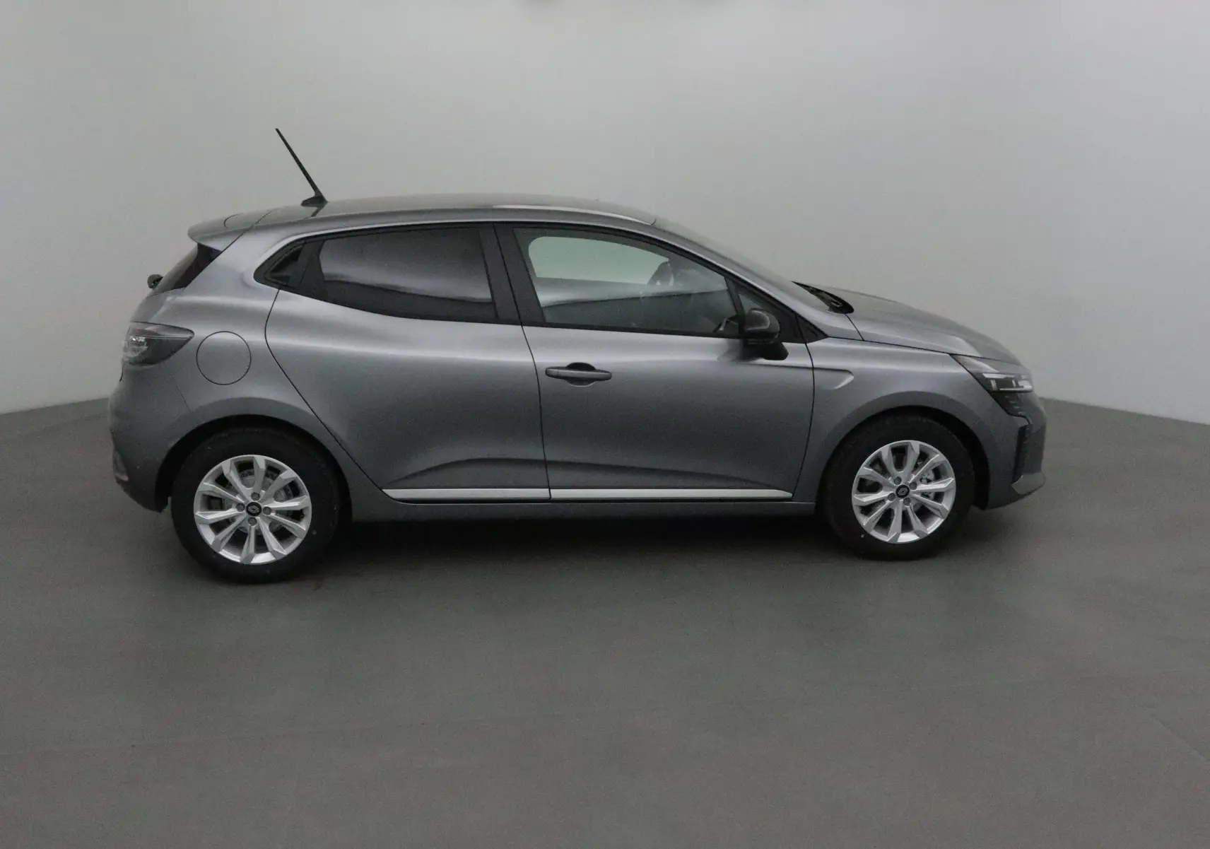 Profil côté gauche d'une Renault Clio V gris schiste 2025 avec protections latérales chromées en intérieur neutre.