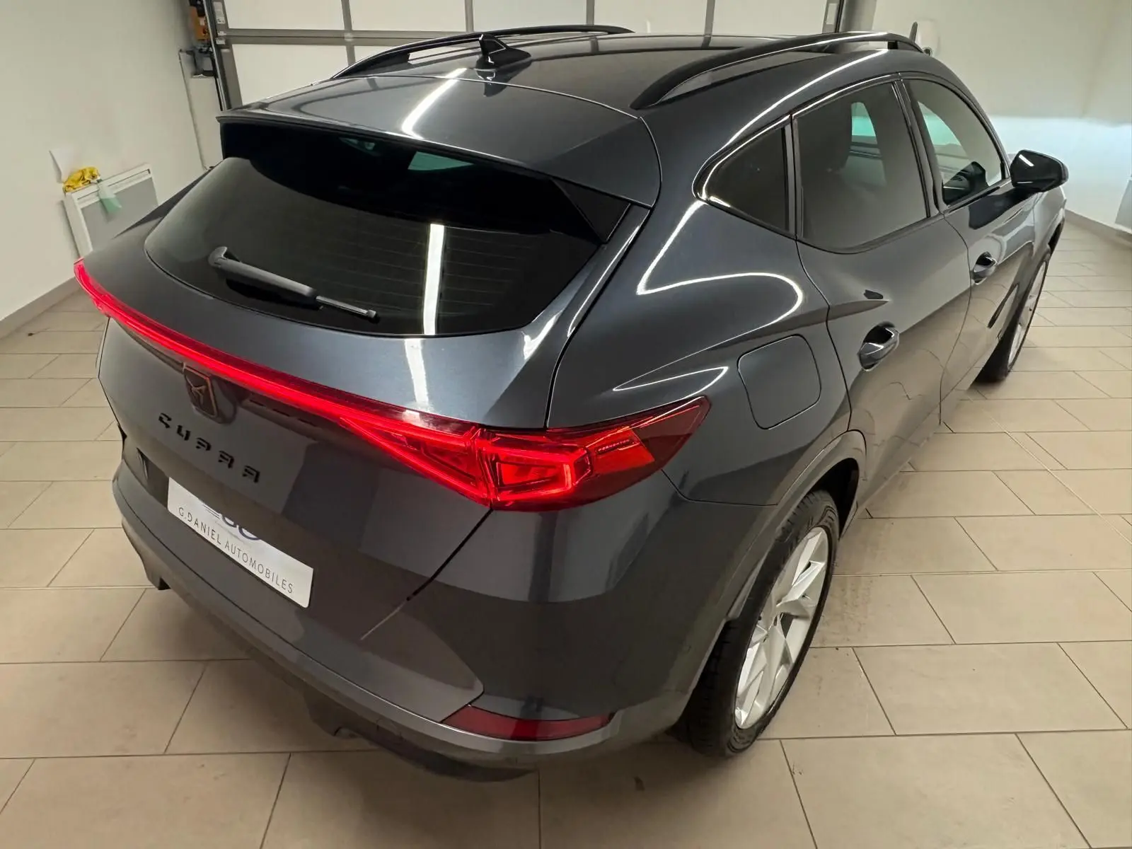 Vue 3/4 arrière droite du CUPRA Formentor gris magnétique 2024 avec feux arrière allumés et toit noir brillant.