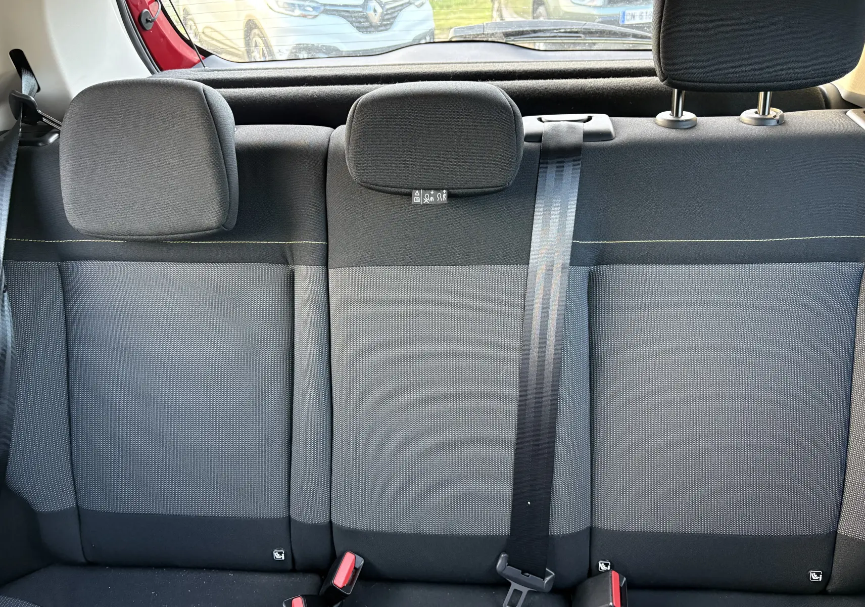 Vue intérieure sur la banquette arrière grise et noire d'une Citroën C3 rouge, avec appuie-têtes et ceinture de sécurité visible.