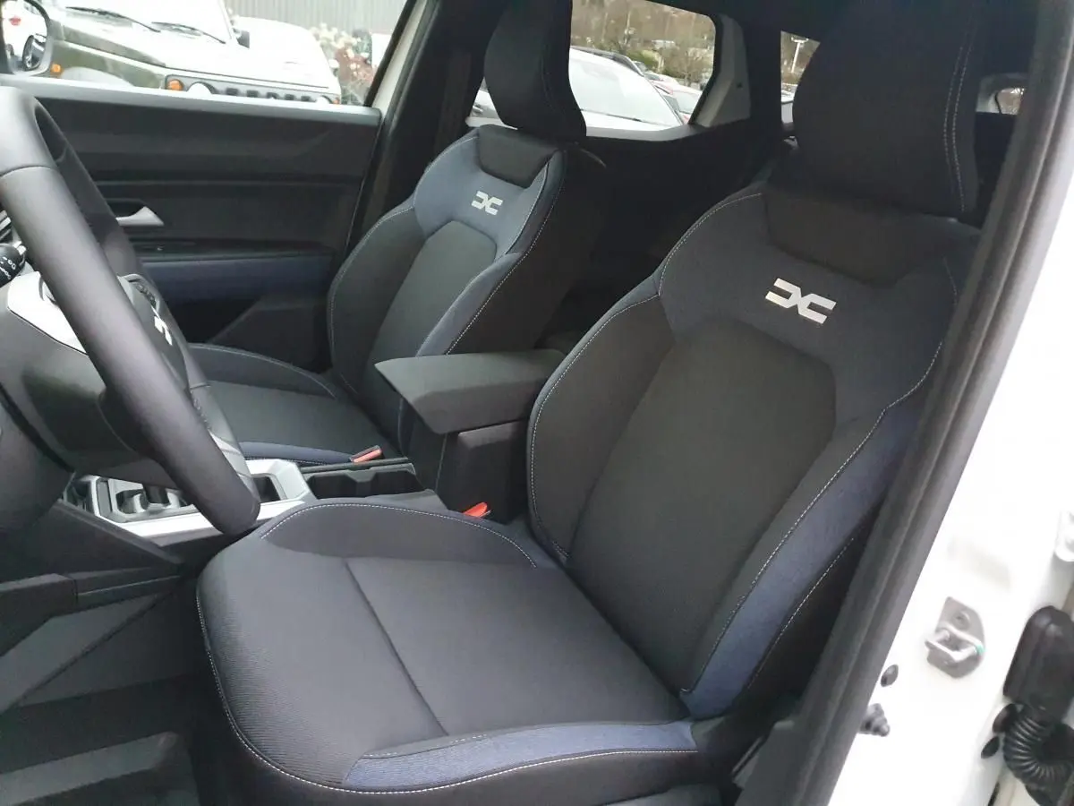 Vue intérieure côté conducteur du Dacia Duster blanc glacier 2025, sièges noirs avec logo distinctif brodé.