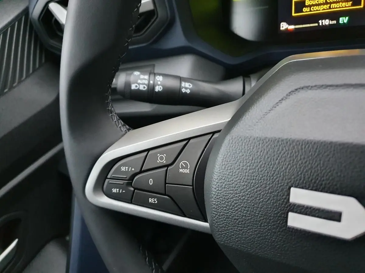 Gros plan sur les commandes au volant côté gauche du Dacia Duster blanc Glacier, affichage numérique en arrière-plan.