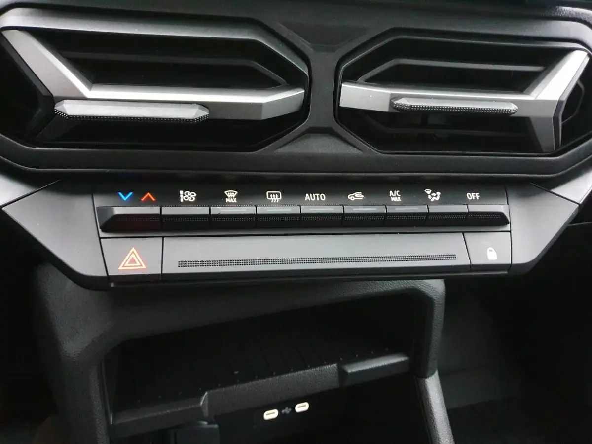 Vue rapprochée du tableau de bord du Dacia Duster blanc glacier 2025, montrant les commandes de climatisation et deux prises USB type C.