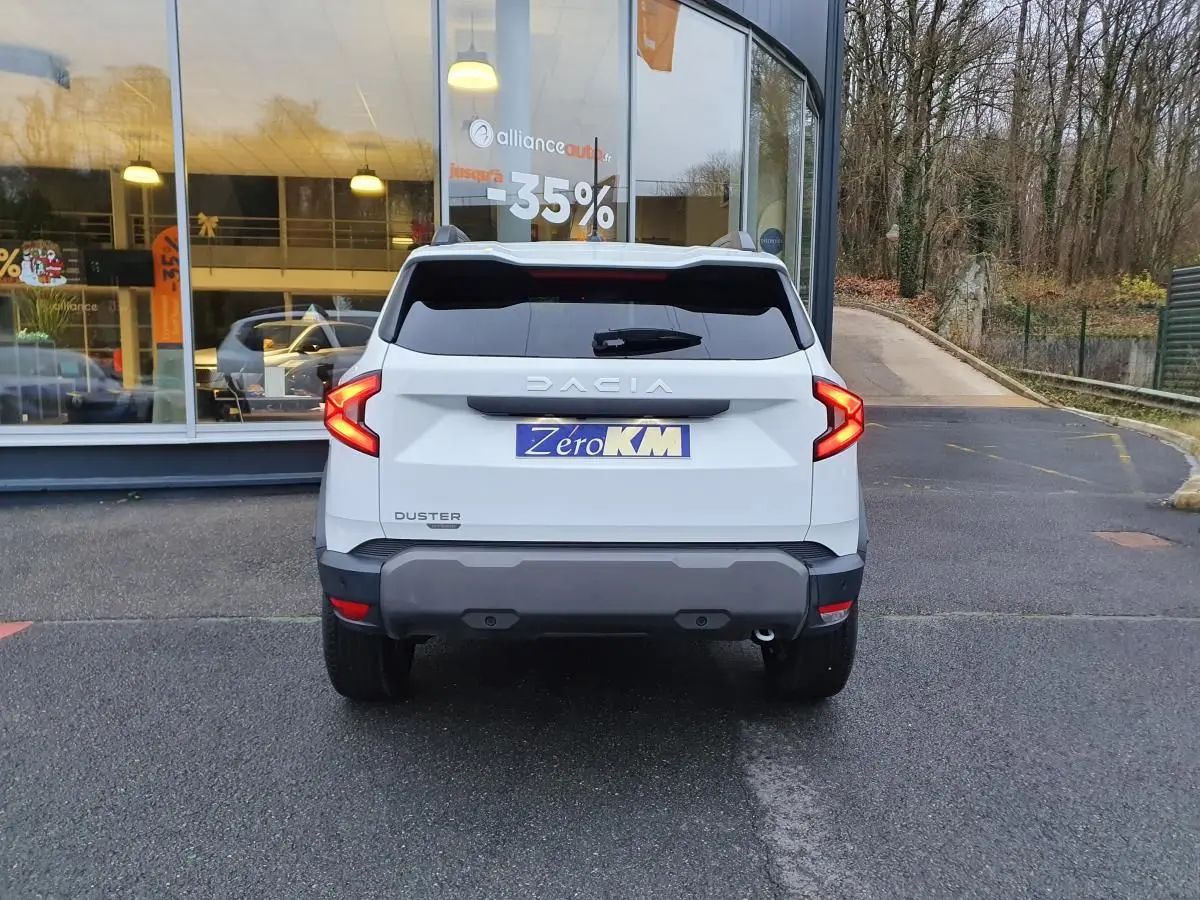 Vue arrière d'un Dacia Duster blanc glacier 2025 avec feux LED en forme de C et vitres arrière surteintées.