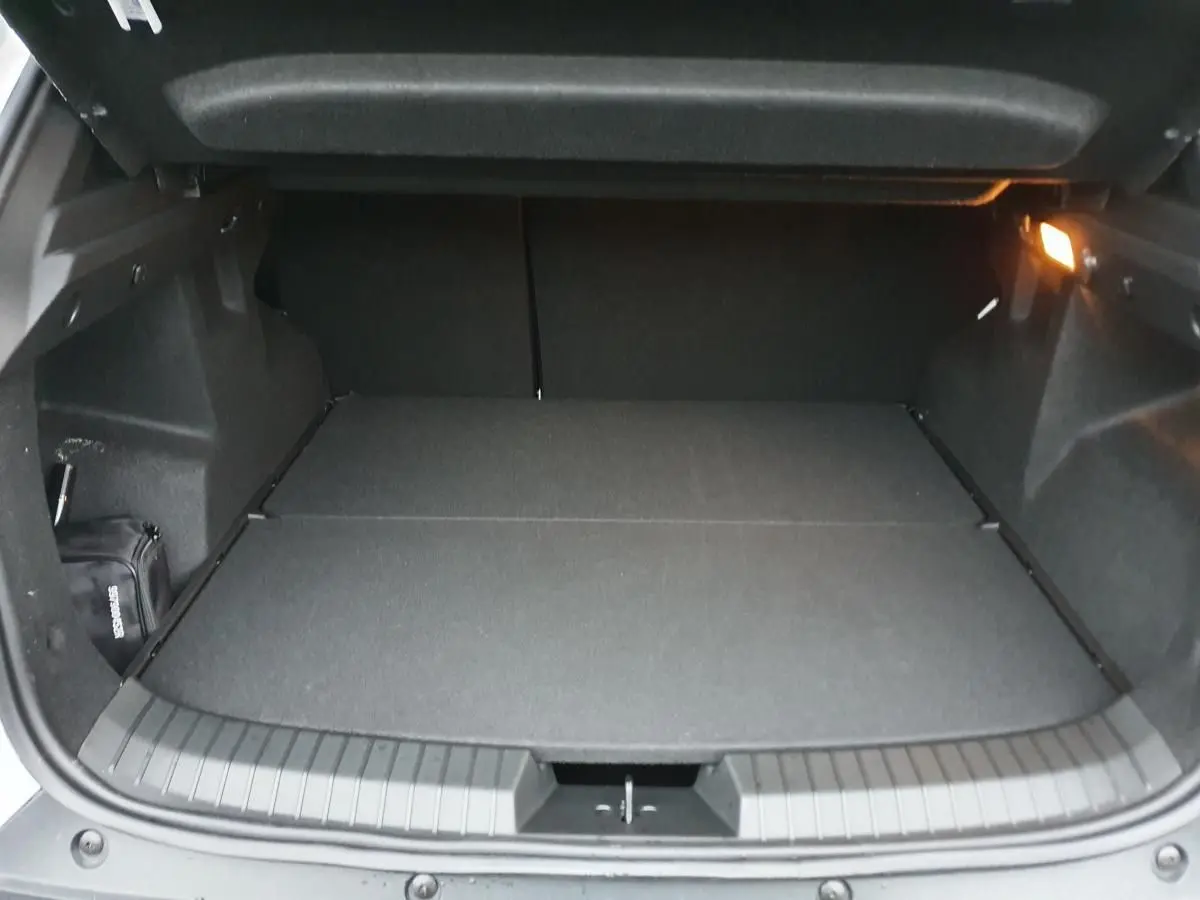 Coffre ouvert du Dacia Duster blanc glacier 2025, vue arrière montrant un espace de chargement plat et éclairé.