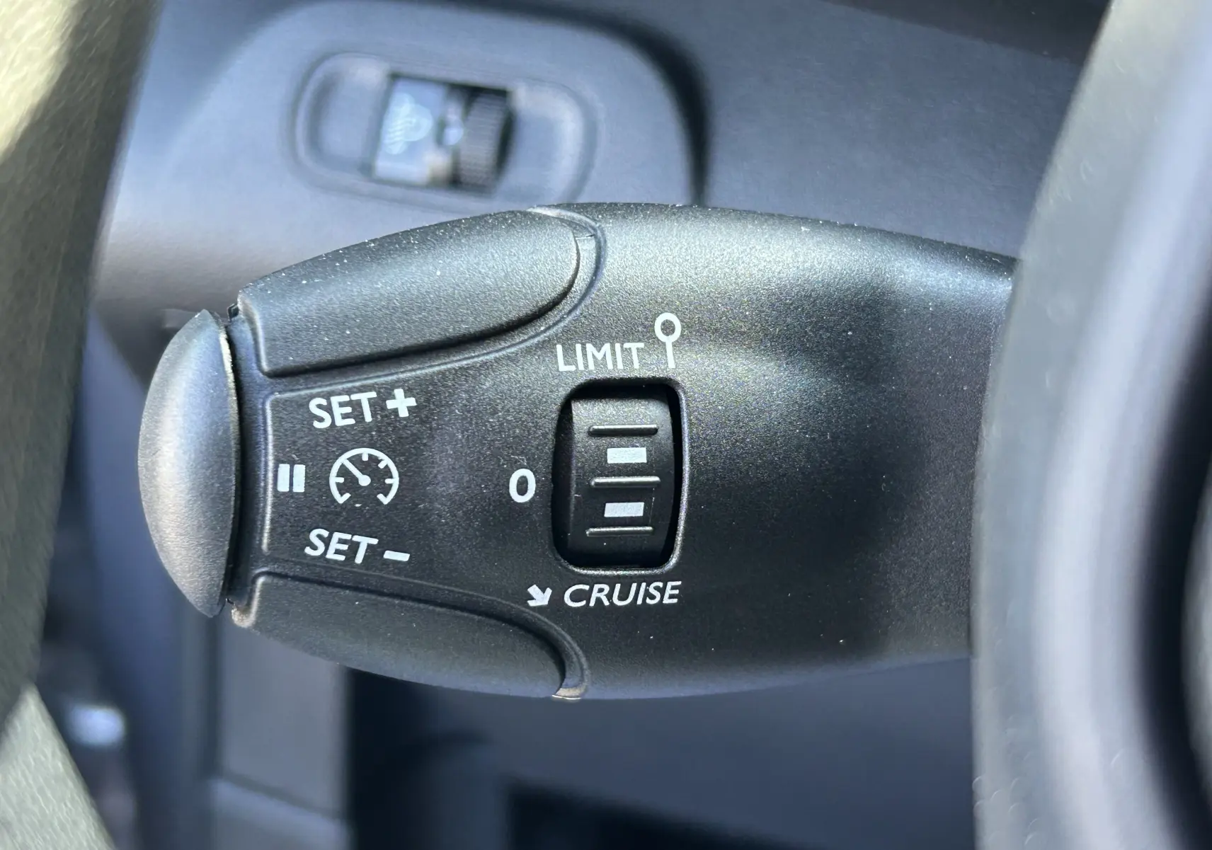 Gros plan sur la commande de régulateur de vitesse du Peugeot Partner Dangel gris Artense, côté gauche du volant.