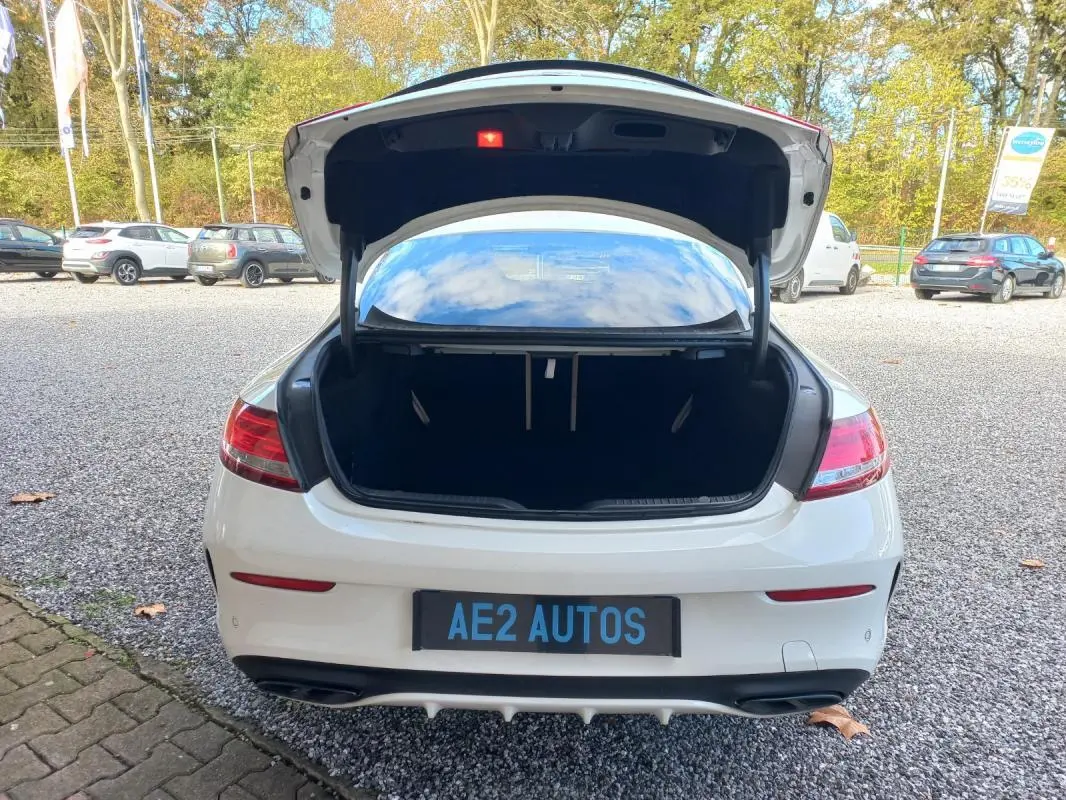 Vue arrière d'une Mercedes Classe C Coupé blanche 2016 avec coffre ouvert sur un parking extérieur.