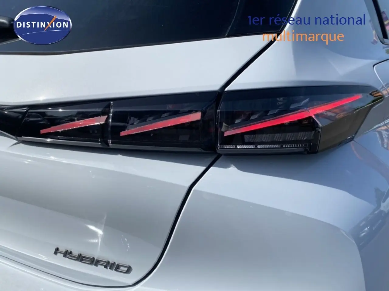 Gros plan sur le feu arrière droit et le logo Hybrid d'une Peugeot 308 blanche Okenite Metal, version hybride 2026.