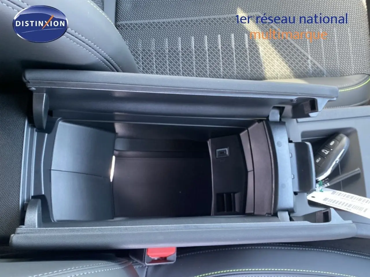 Vue plongeante sur le rangement central ouvert de la Peugeot 308 Hybrid 145ch GT, intérieur noir avec surpiqûres vertes.
