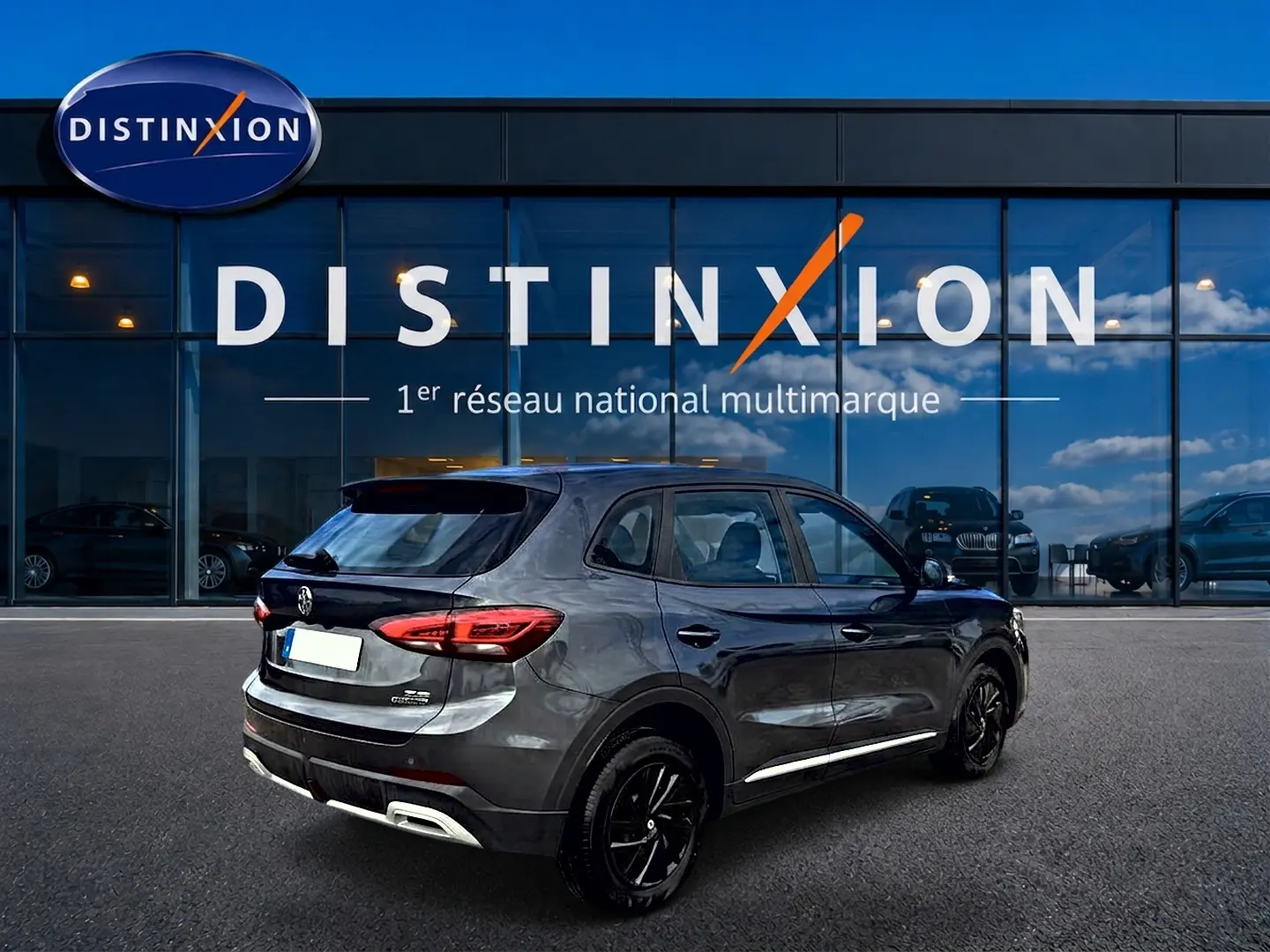 Vue 3/4 arrière droite du MG ZS Camden grey 2026 hybride, avec feux LED et jantes noires devant une vitrine Distinxion.