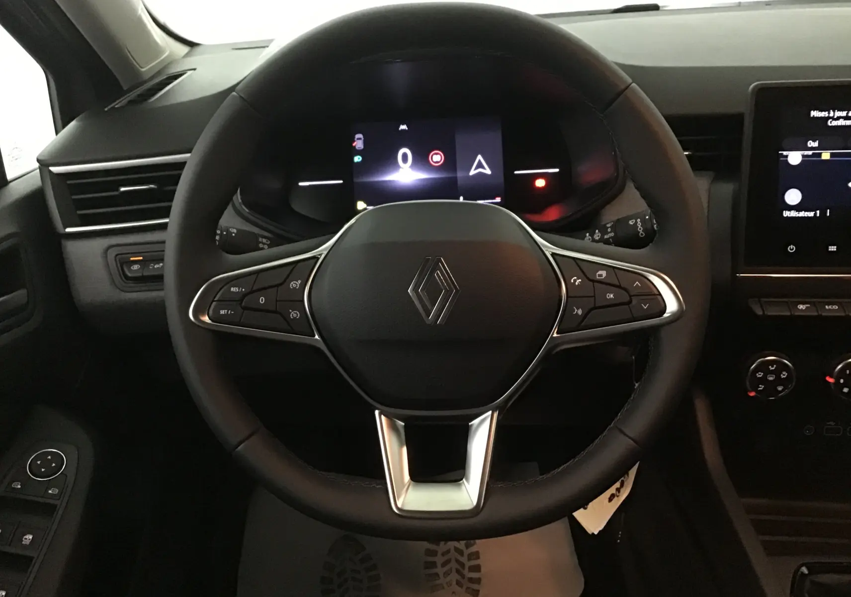 Vue rapprochée du volant noir de la Renault Clio V 1.5 DCI 100 Evolution avec tableau de bord numérique allumé.