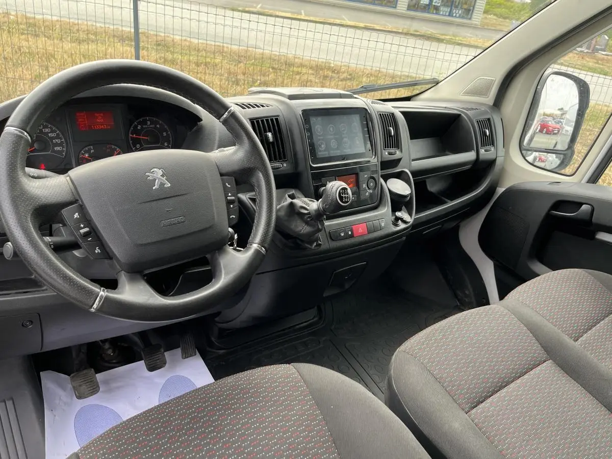 Vue intérieure côté conducteur du Peugeot Boxer Fourgon 2023, montrant le volant cuir, tableau de bord et console centrale noire.
