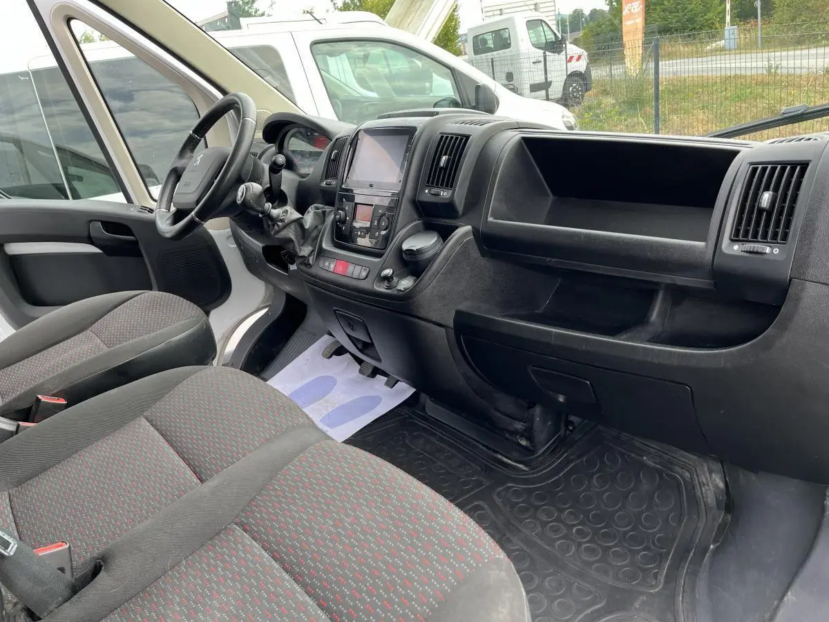 Vue intérieure côté conducteur du Peugeot Boxer Fourgon 2023, tableau de bord noir et sièges tissu gris à motifs rouges.