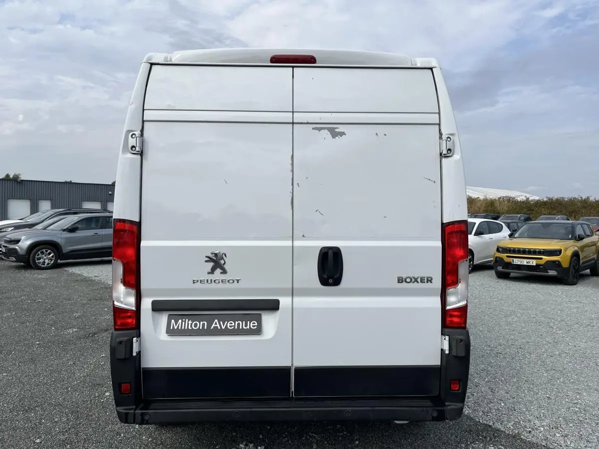 Vue arrière d'un utilitaire Peugeot Boxer blanc avec portes tôlées et feux rouges verticaux.