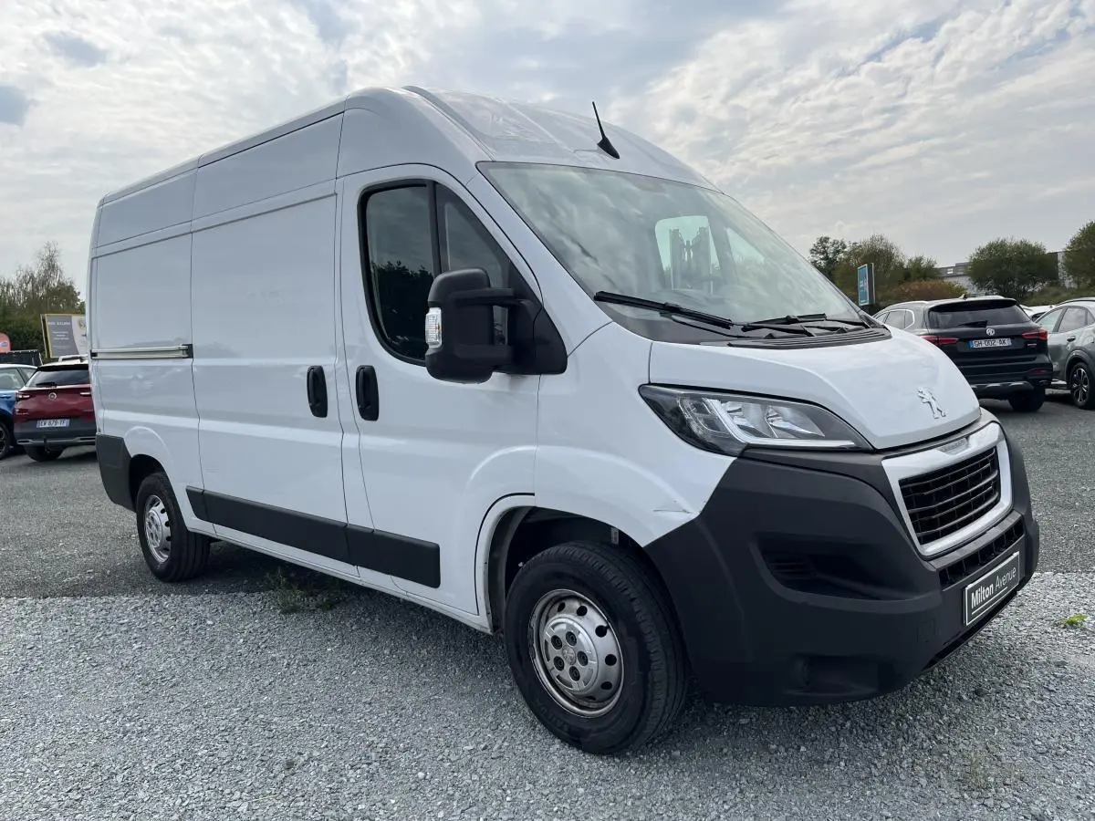 Fourgon utilitaire Peugeot Boxer blanc vu en 3/4 avant droit avec pare-chocs noirs et porte latérale coulissante.