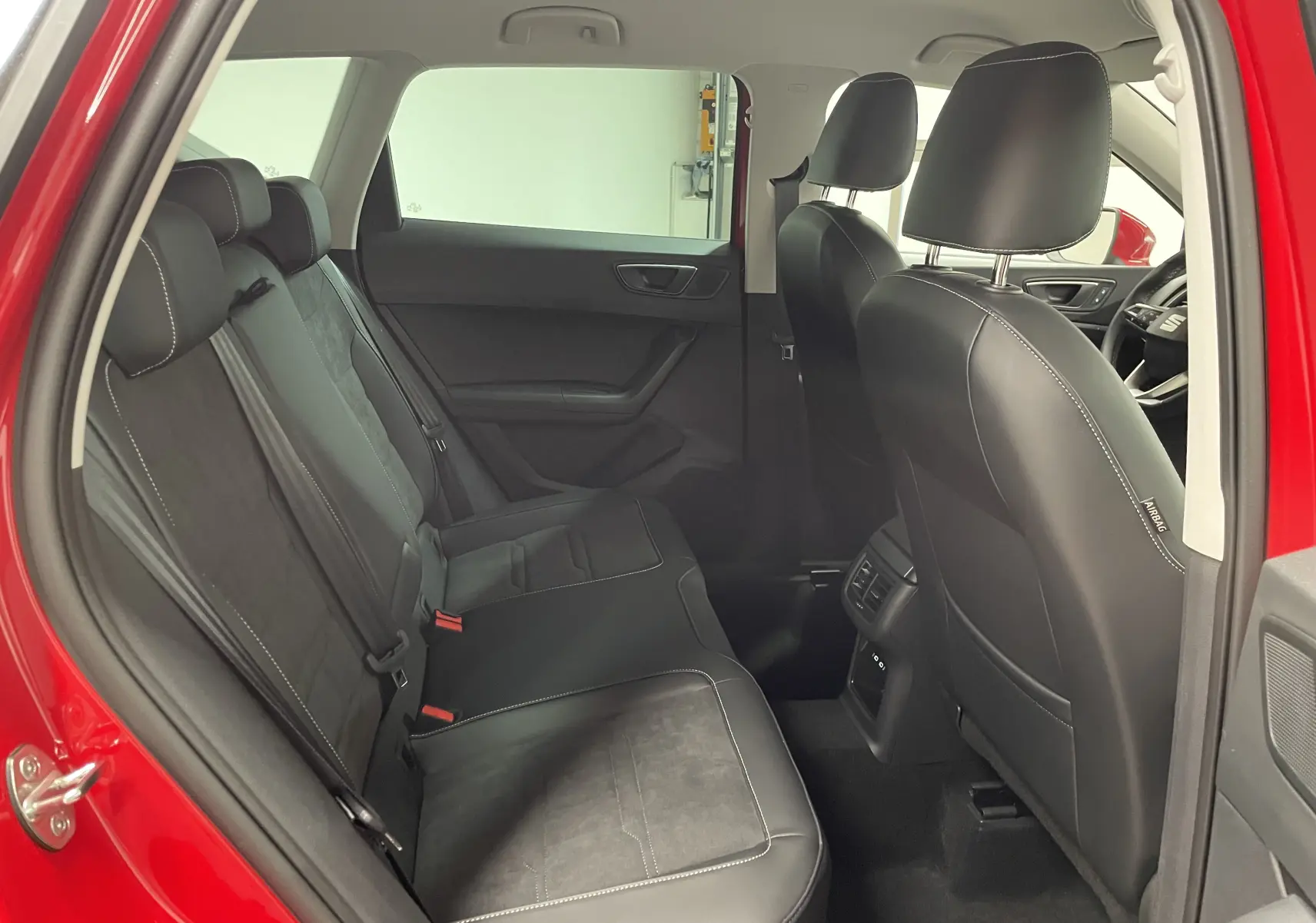 Vue intérieure arrière côté gauche du SEAT Ateca Rouge Velvet 2024, montrant les sièges en cuir noir avec surpiqûres blanches.