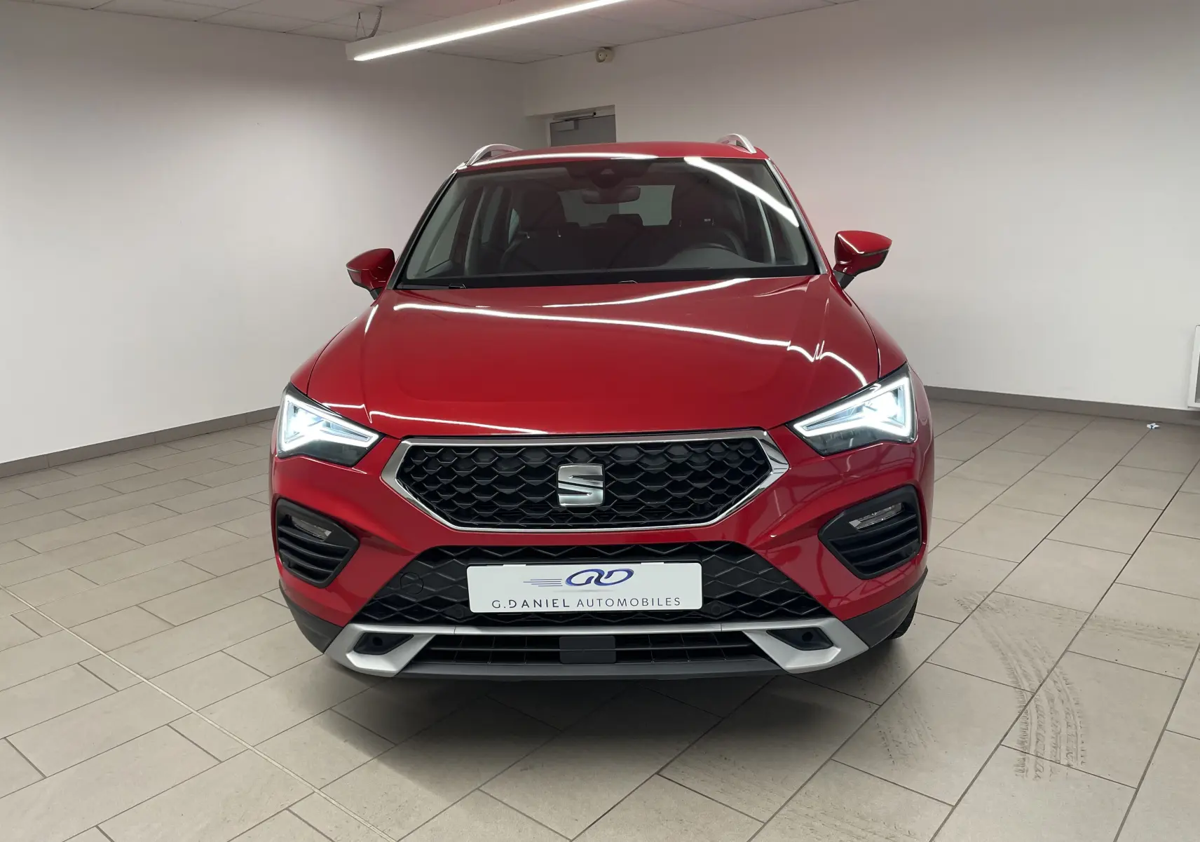 Vue frontale d'un SEAT Ateca 2024 en rouge Velvet métallisé avec phares allumés et calandre noire hexagonale.
