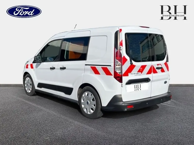 Vue 3/4 arrière droite du Ford Transit Connect blanc glacier avec bandes réfléchissantes rouges et portes arrière vitrées.