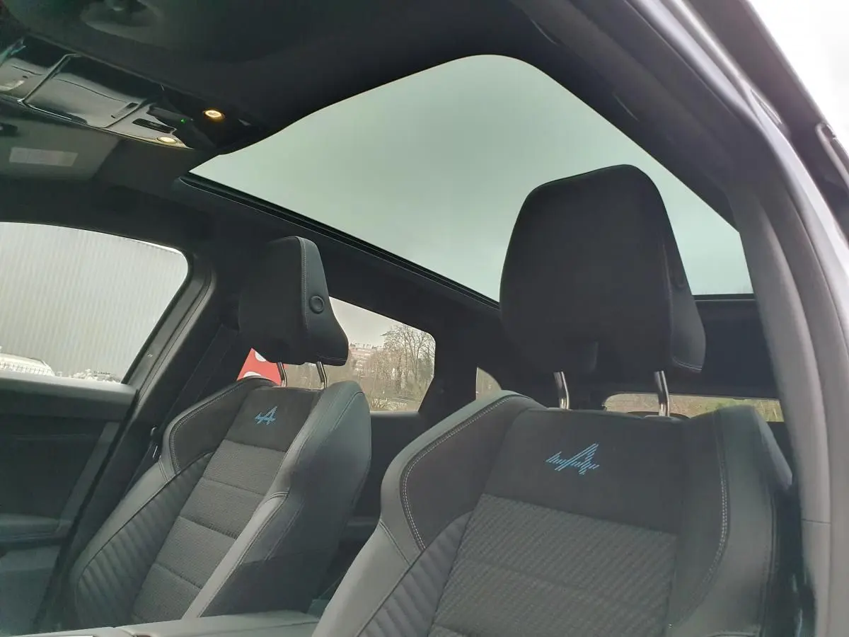 Vue intérieure des sièges avant en tissu carbone Alcantara gris avec logo Alpine bleu, toit panoramique en verre noir visible.