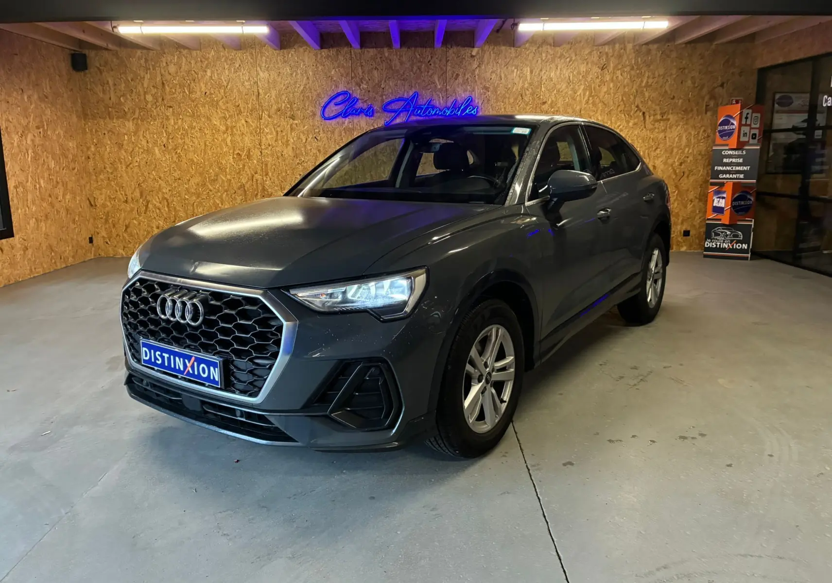 Audi Q3 Sportback gris en vue 3/4 avant droit, avec calandre hexagonale et jantes 17 pouces cinq branches doubles.