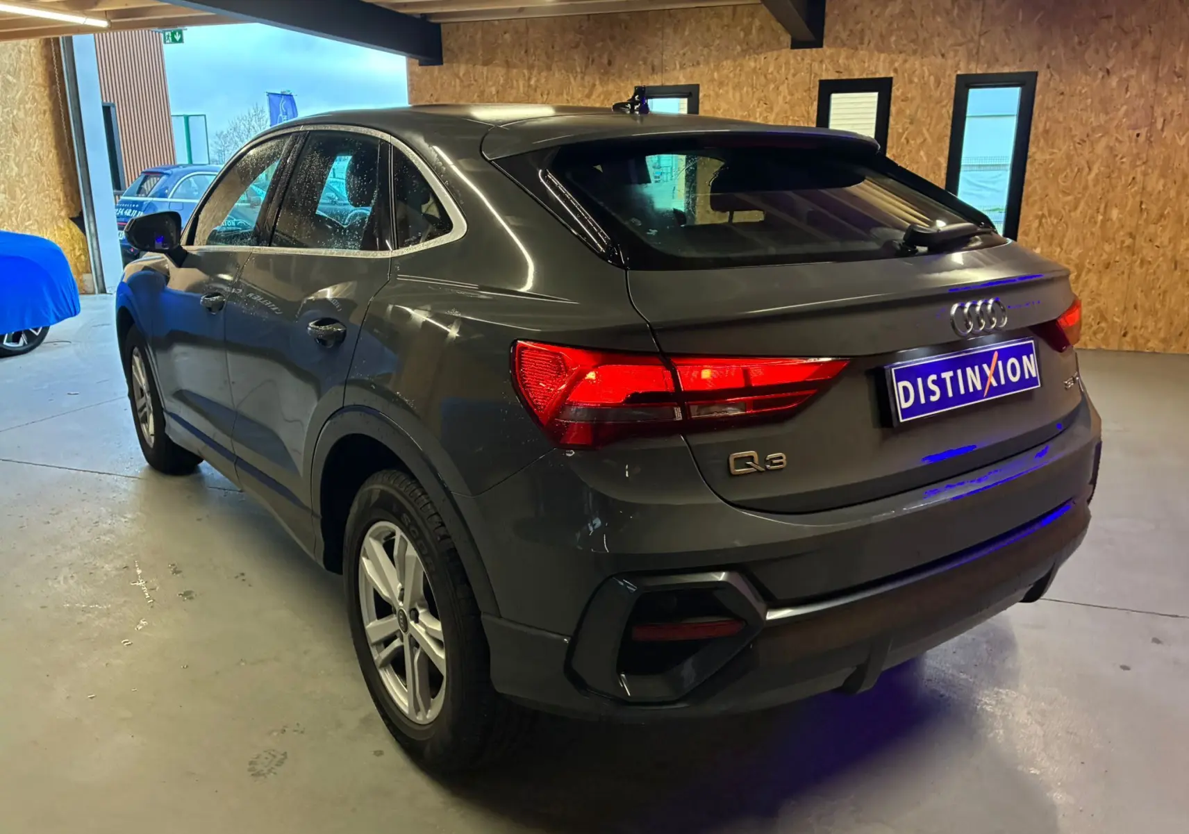 Audi Q3 Sportback gris vue 3/4 arrière droit, avec feux arrière allumés dans un garage.