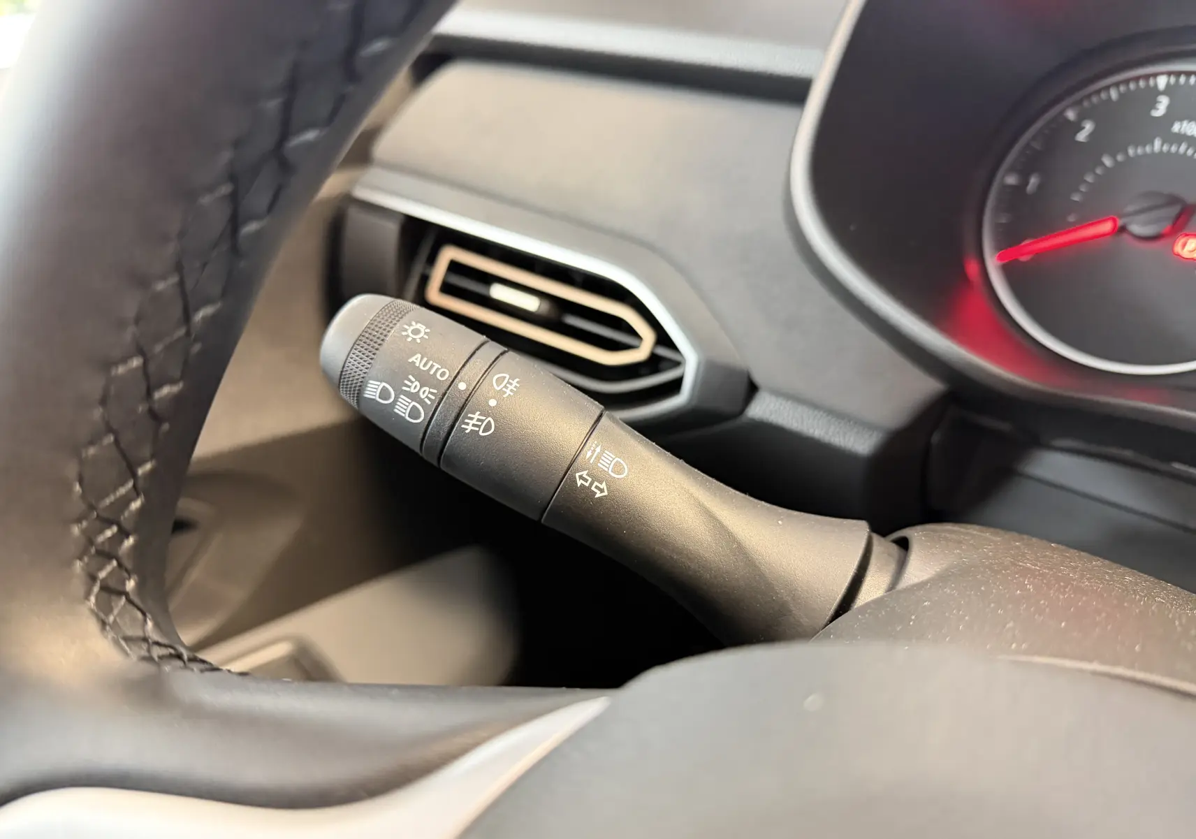Gros plan sur la manette des feux et clignotants à gauche du volant dans l’habitacle noir du Dacia Jogger gris schiste.