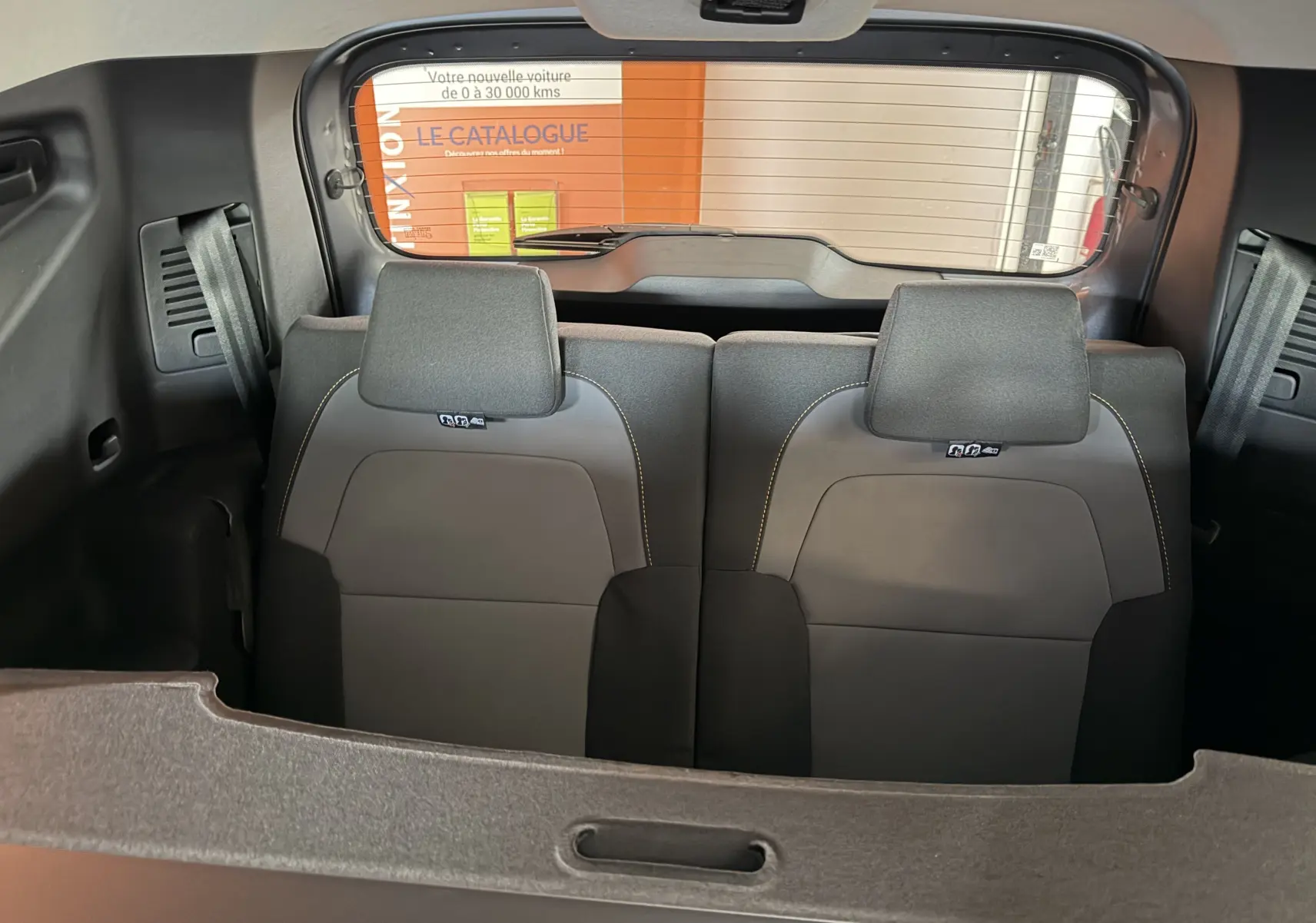 Vue intérieure arrière du Dacia Jogger 2026, sièges gris avec appuie-têtes et ceintures visibles, arrière vitré et cache-bagages.