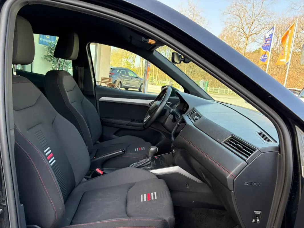 Vue intérieure côté conducteur du SEAT Arona noir 2020, montrant les sièges sport avec surpiqûres rouges et tableau de bord épuré.