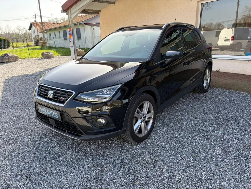 SEAT Arona noir vue 3/4 avant droit, avec calandre hexagonale et jantes alliage, stationné sur gravier devant un bâtiment.