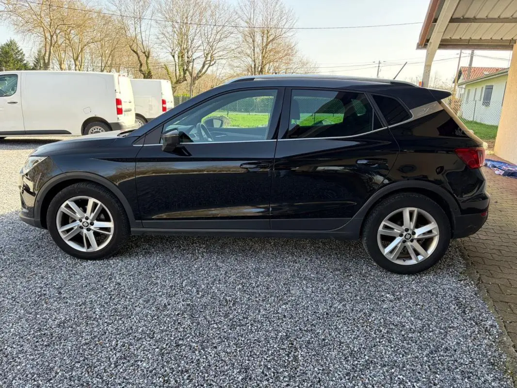 Vue de profil côté gauche d’un SEAT Arona noir 2020 garé sur un sol gravillonné avec jantes alliage visibles.