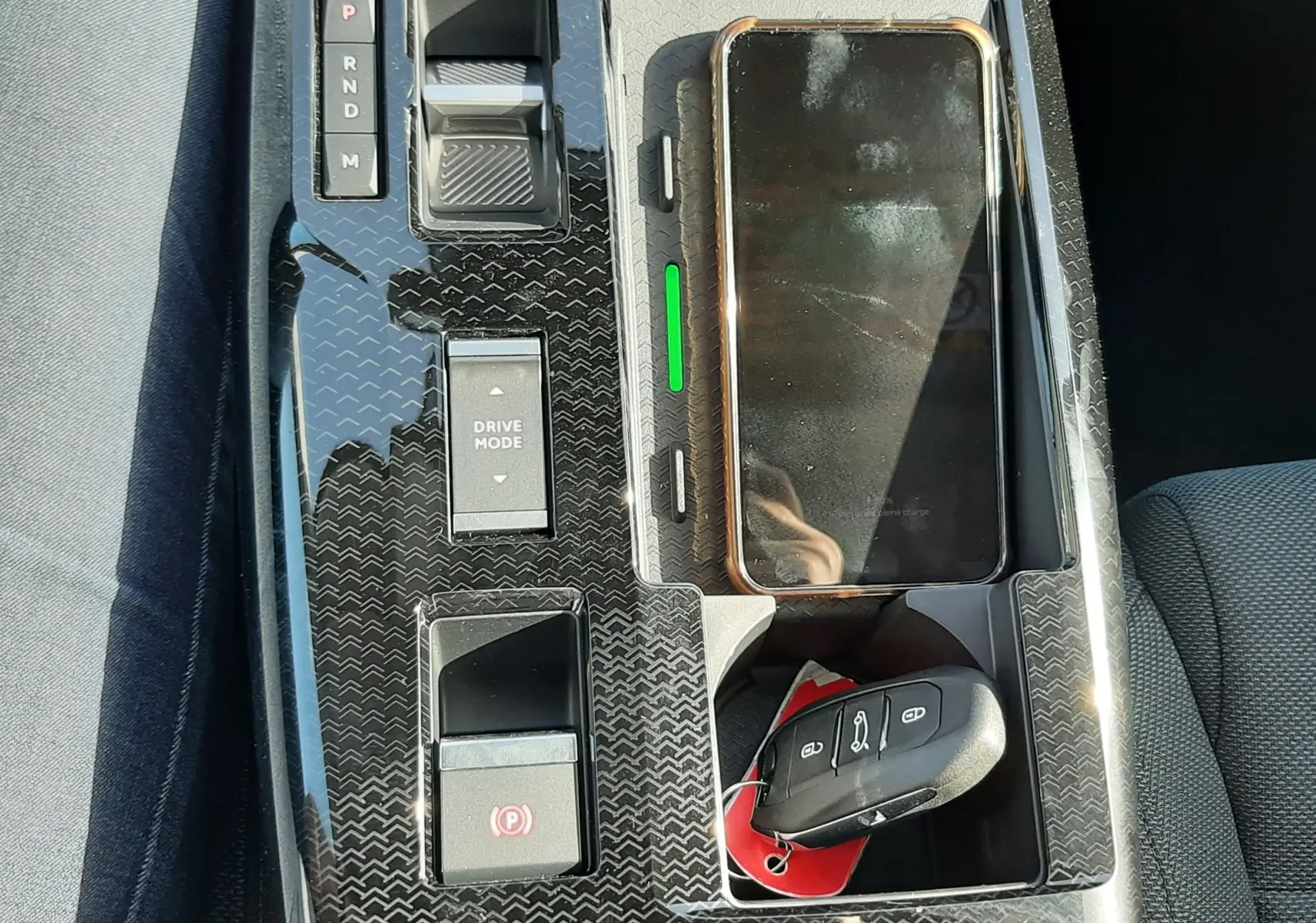 Vue plongeante sur la console centrale noire brillante du Citroën C5 Aircross hybride, avec clé et smartphone posés.