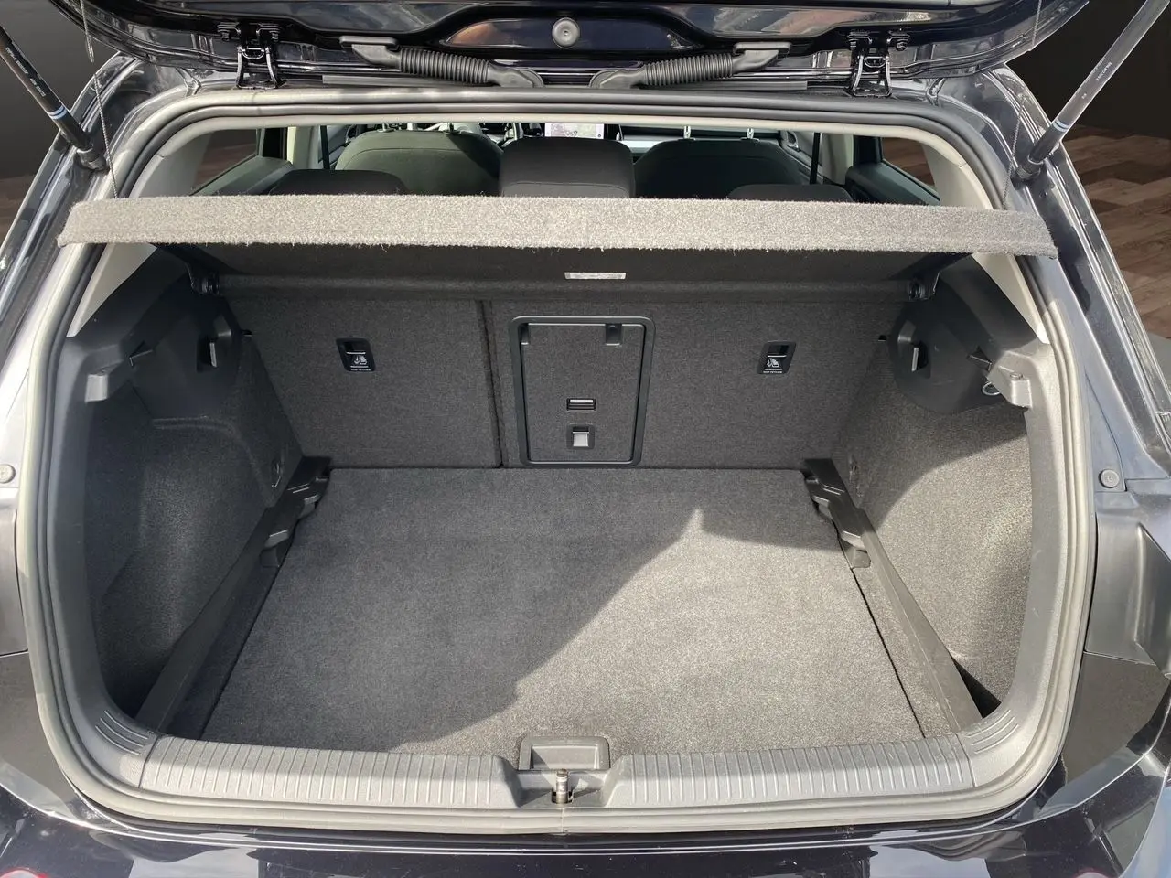 Coffre ouvert d'une Volkswagen Golf VIII noire vue de l'arrière, montrant un espace de chargement propre et spacieux.
