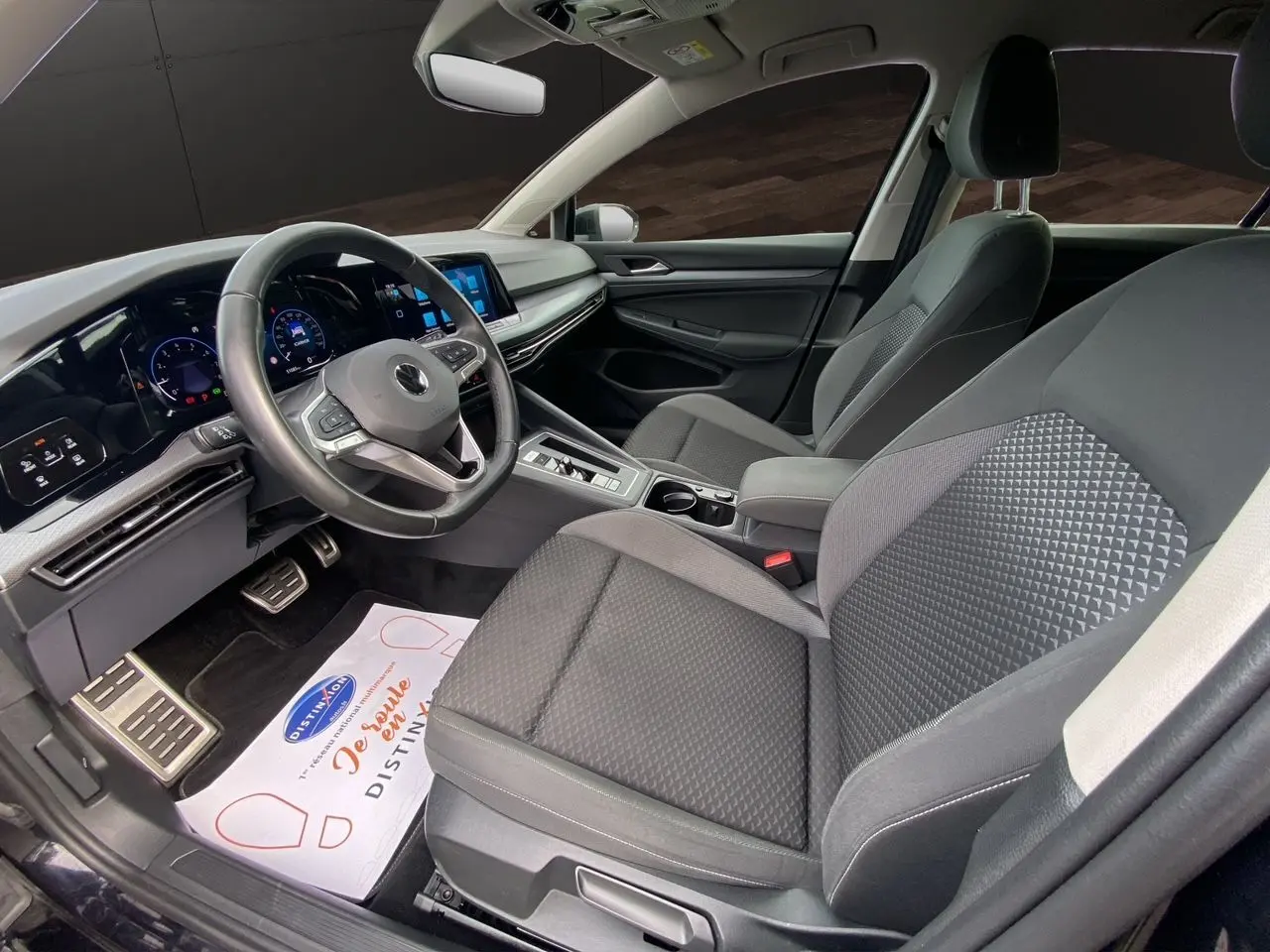 Intérieur noir de la Volkswagen Golf VIII vue côté conducteur, avec tableau de bord numérique et sièges tissu gris foncé.