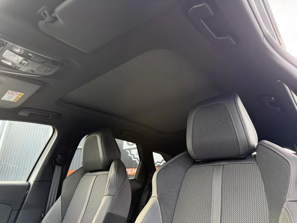 Détail intérieur montrant le toit ouvrant panoramique et les sièges avant gris du Peugeot 3008 Hybrid 2023.