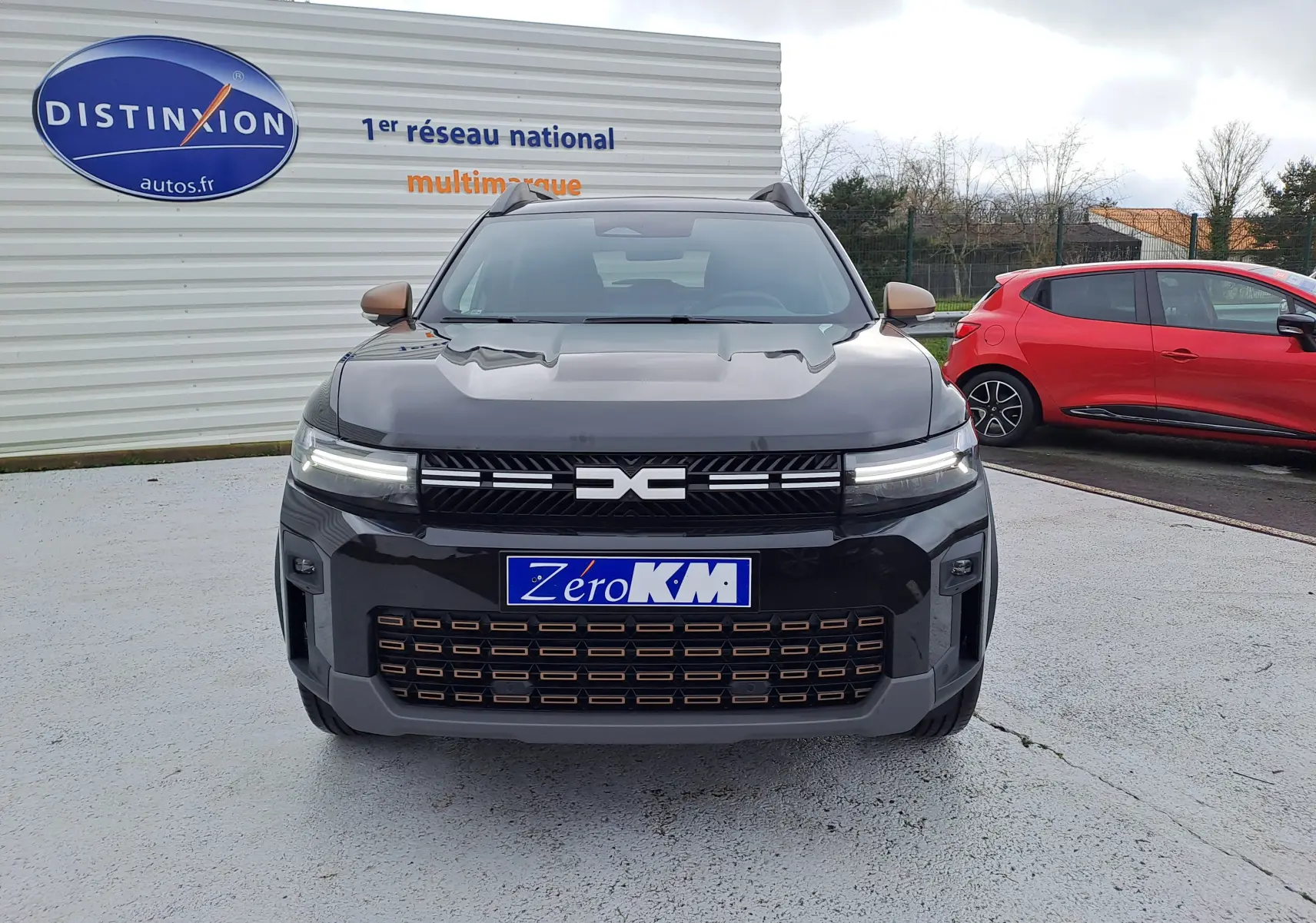 Vue avant d'un Dacia Bigster noir nacré avec calandre marquée et phares LED fins, stationné devant un mur publicitaire.