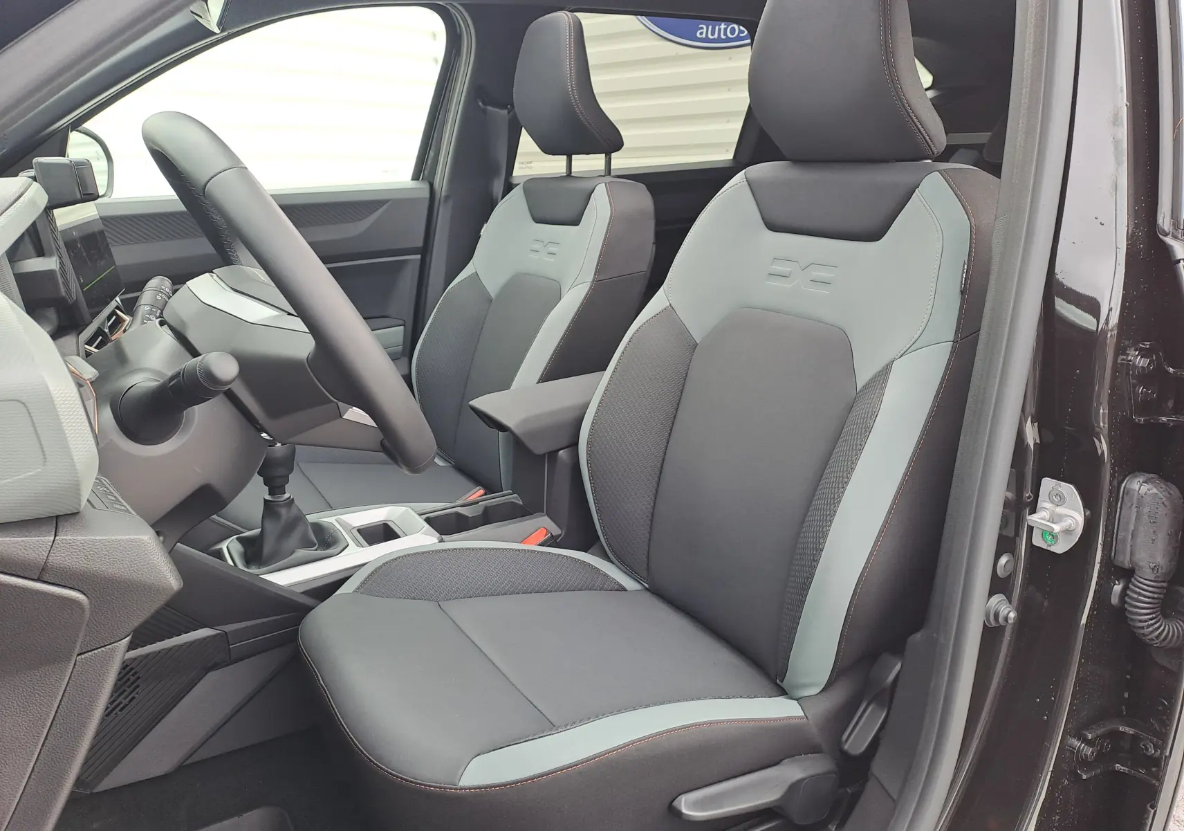 Vue intérieure côté conducteur du Dacia Bigster noir nacré 2025, sièges bi-ton gris et noir avec logo brodé.