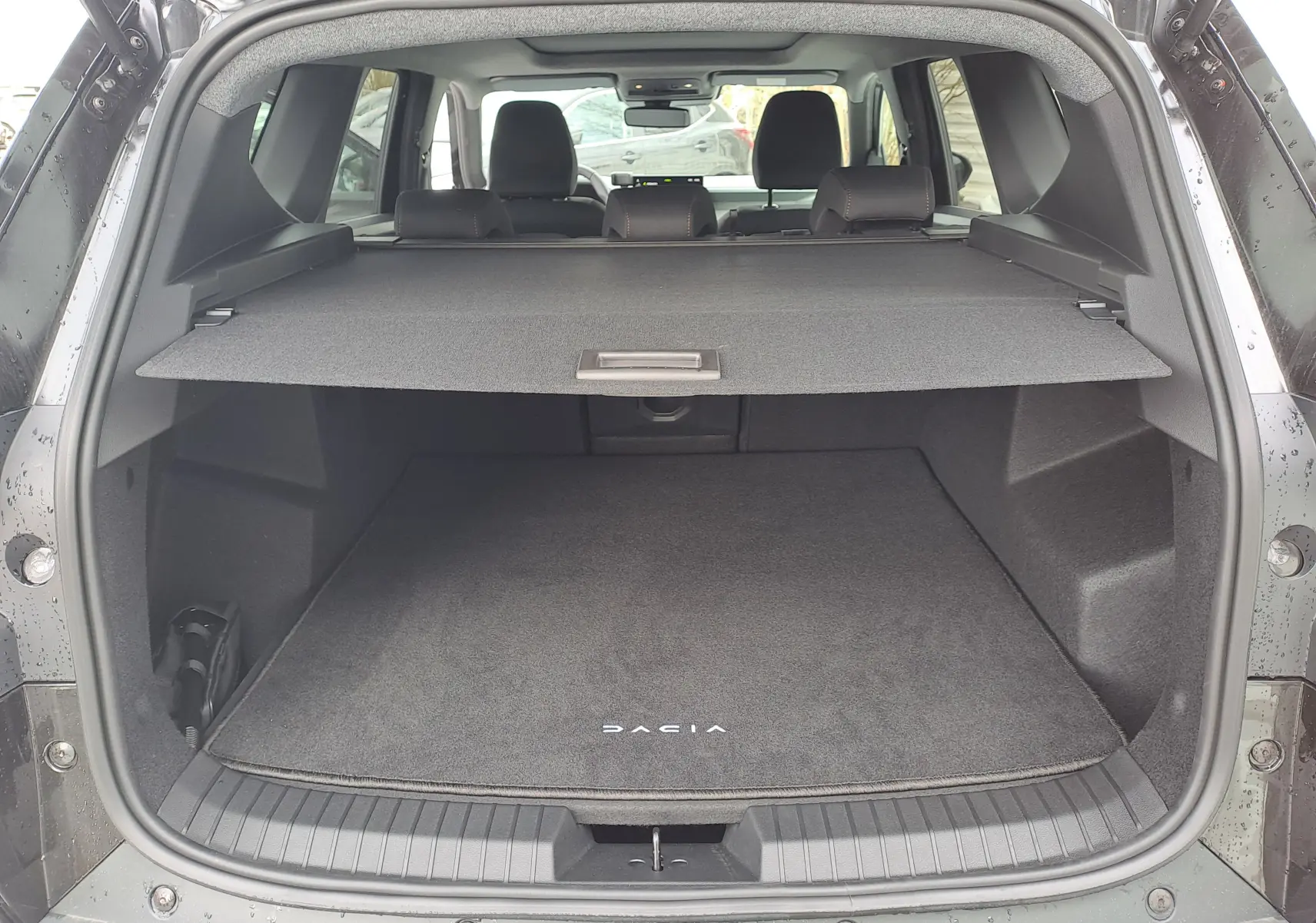 Vue arrière du coffre ouvert du Dacia Bigster noir nacré, avec cache-bagages et tapis de sol marqué Dacia.
