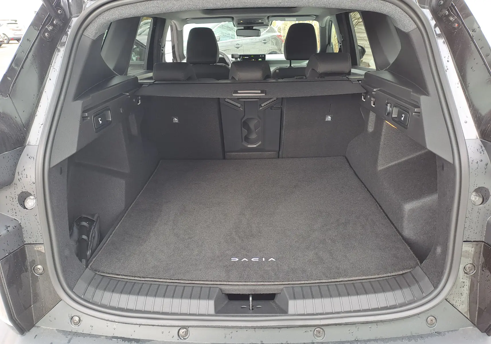 Coffre ouvert vu de l'arrière d'un Dacia Bigster noir nacré, avec tapis de sol marqué Dacia et banquette arrière visible.