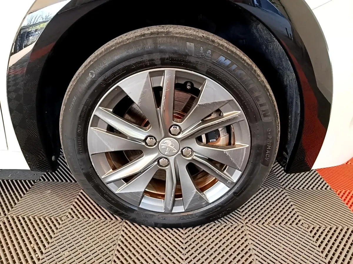 Gros plan sur la roue avant droite d'une Peugeot 208 électrique blanche, jante alliage à cinq doubles branches.