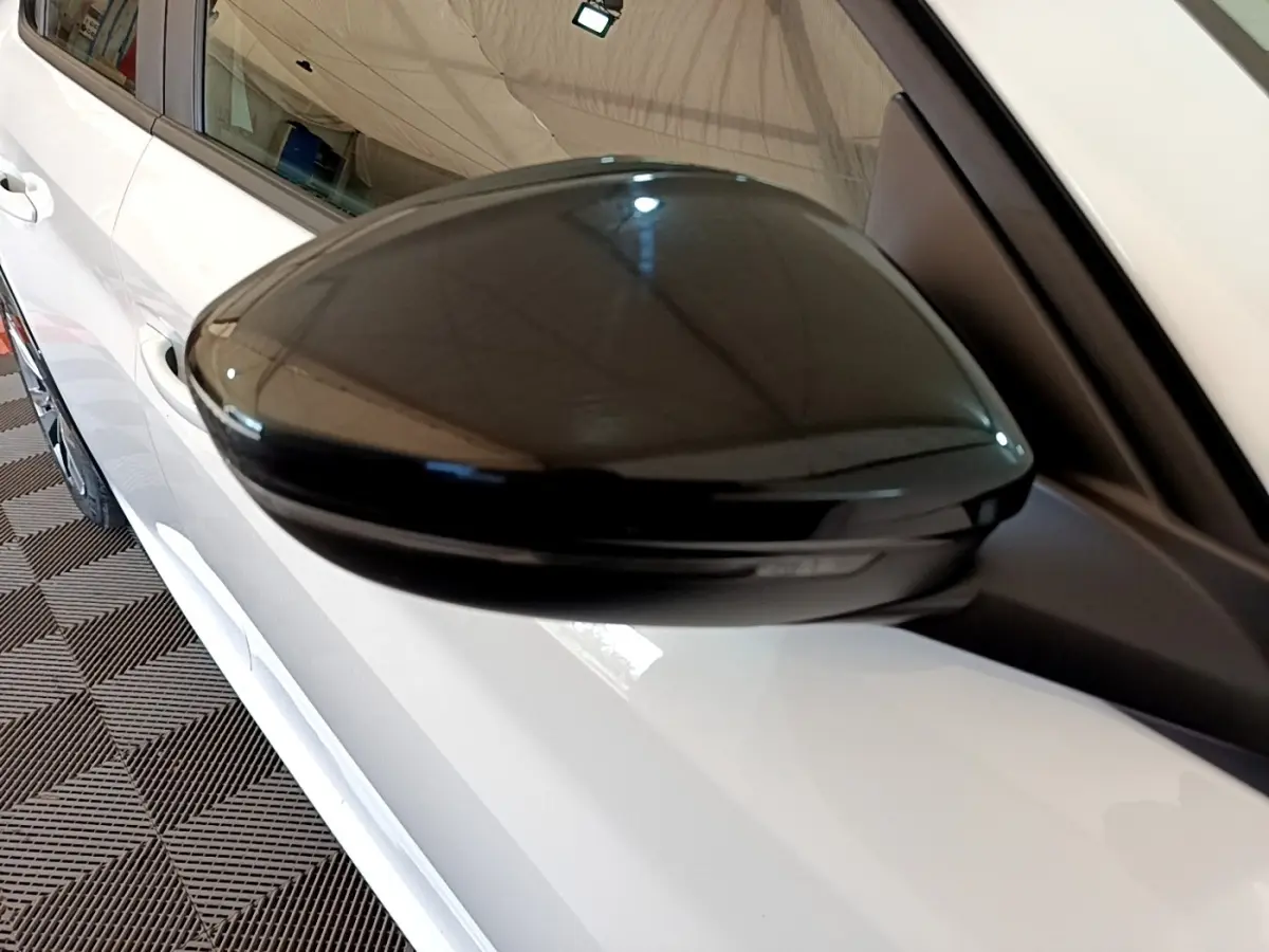 Gros plan sur le rétroviseur noir côté droit d'une Peugeot 208 électrique blanche, vue partielle latérale.