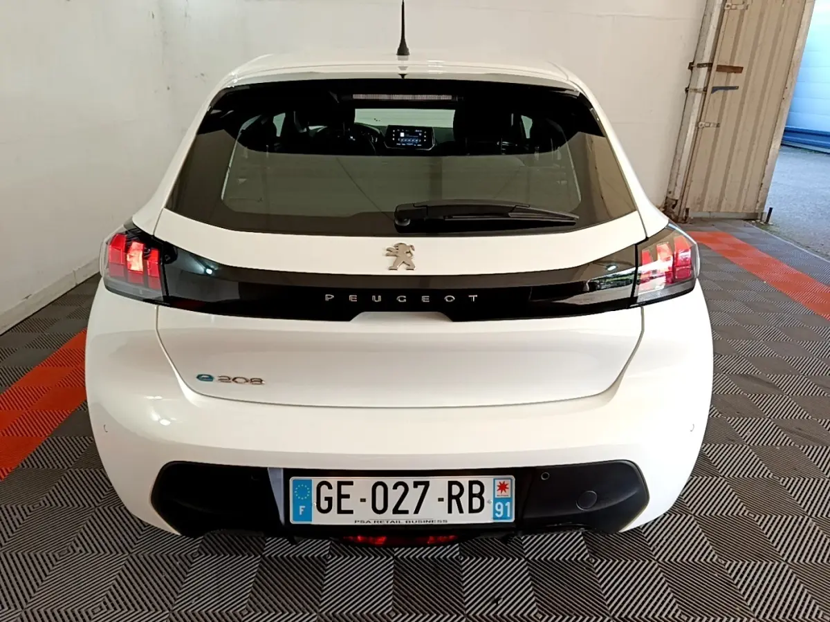 Vue arrière d'une Peugeot 208 électrique blanche avec bande noire et feux arrière allumés en intérieur.