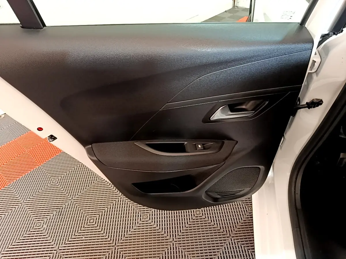 Vue intérieure sur la porte arrière droite noire d’une Peugeot 208 électrique blanche de 2022, avec poignée et commande vitre.