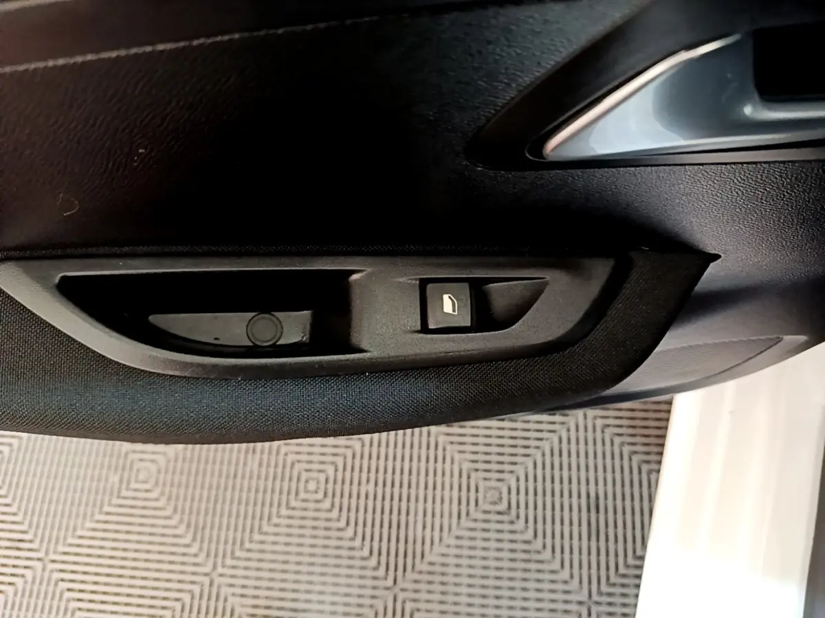 Détail de la commande de lève-vitre côté conducteur sur la porte intérieure d’une Peugeot 208 électrique blanche.