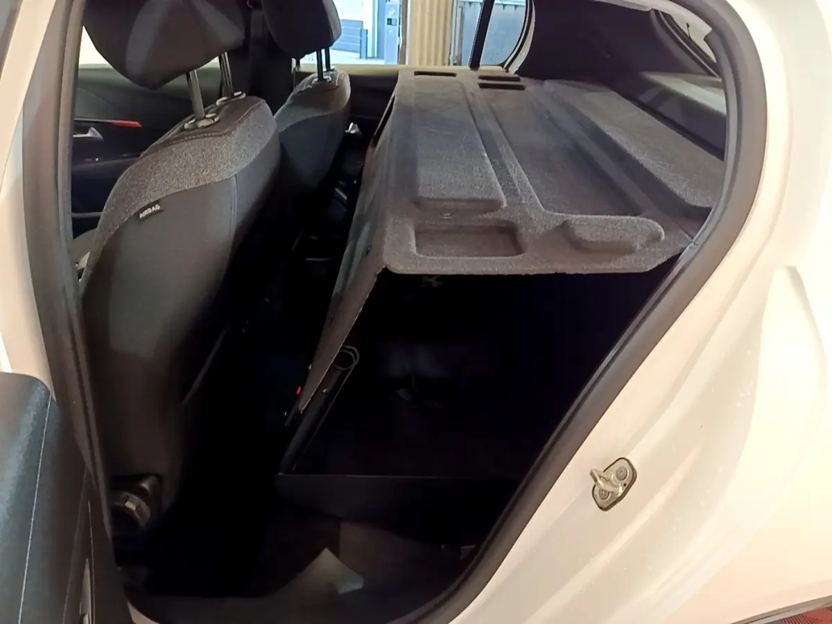 Vue côté droit arrière d'une Peugeot 208 électrique blanche avec banquette arrière rabattue et coffre ouvert.