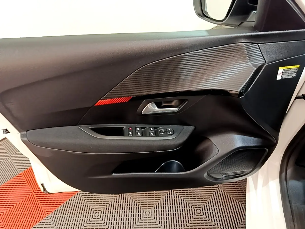 Vue intérieure sur la porte avant gauche blanche d’une Peugeot 208 électrique avec garniture noire et insert effet carbone.